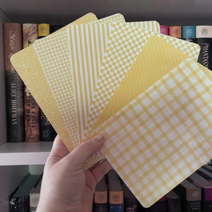 May include: A set of rectangular cards featuring various yellow and white patterns, including gingham, stripes, checkered, and speckled designs, fanned out to display the different textures and prints on each individual card surface.
