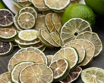 May include: Dried lime slices, some whole limes, and a bowl of lime slices on a dark wood surface. The lime slices are a light brown colour with a green rim.