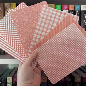 May include: A set of rectangular cards featuring various patterns in shades of coral and white, including stripes, a checkerboard design, a speckled texture, a plaid pattern, and a small gingham check, all held together in a fan shape.