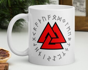 May include: White ceramic mug with a red Valknut symbol surrounded by a circle of Norse runes. The runes are in grey and spell "Hávamál".