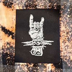 May include: Black and white iron-on patch with a hand making the rock and roll hand gesture. The hand is surrounded by barbed wire.
