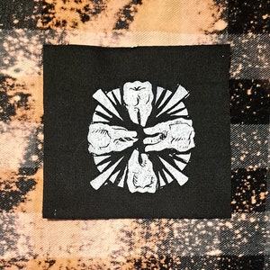 May include: Black iron-on patch with a white graphic of five teeth in a circle with rays emanating from the centre.