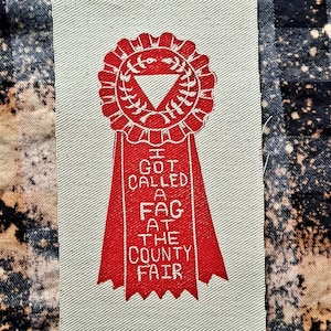 Peut inclure: Patch en tissu rouge avec un ruban blanc et le texte "I GOT CALLED A FAG AT THE COUNTY FAIR".