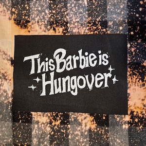 May include: A black patch with white text that reads "This Barbie is Hungover" on a bleached plaid background.