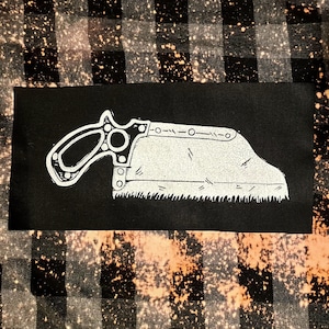 Peut inclure: Une silhouette blanche d'une scie à main sur un fond noir. La scie a une poignée en bois et une lame en métal avec des dents.