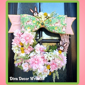 May include: A pink and green floral wreath with a bow and bunny rabbits. The wreath is decorated with pink flowers, green leaves, and yellow accents. The bow is made of a pink and green fabric with a bunny rabbit pattern. The wreath is hanging on a brown door. The text "Diva Decor Wreaths" is at the bottom of the image.