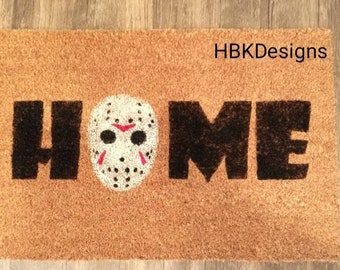 May include: A brown coir doormat with the word "HOME" in black lettering. The "O" is replaced with a white hockey mask with red accents.