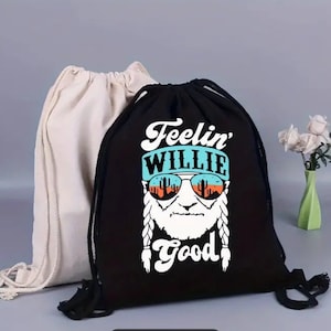 May include: Black drawstring bag with a white graphic of a man with a beard and sunglasses. The graphic says "Feelin' Willie Good".