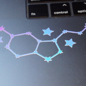 May include: A holographic sticker of a constellation with a hexagonal shape, featuring a gradient of pink, purple, and blue stars on a gray laptop.