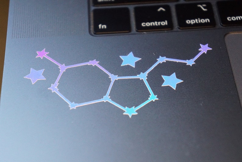 May include: A holographic sticker of a constellation with a hexagonal shape, featuring a gradient of pink, purple, and blue stars on a gray laptop.
