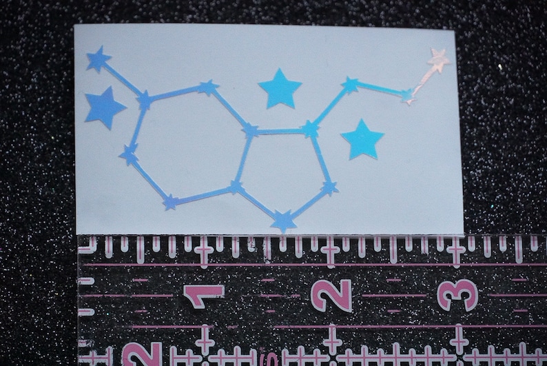 May include: A blue iridescent vinyl sticker of the constellation Gemini. The sticker is on a white background and is approximately 2 inches wide.