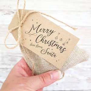 May include: A small burlap gift bag with a brown paper tag tied with twine. The tag reads "Merry Christmas love from Santa" in black script, with star and bauble illustrations.