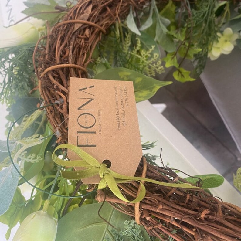 Puede incluir: Una corona verde y marr&oacute;n con una etiqueta marr&oacute;n que dice "Fiona Floral Couture" con informaci&oacute;n de contacto.