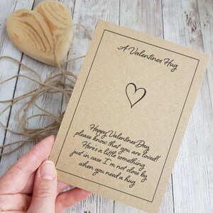 May include: A brown card with the text "A Valentines Hug" and a heart symbol. The card also has the text "Happy Valentines Day, please know that you are loved! Here's a little something just in case I'm not close by when you need a hug."