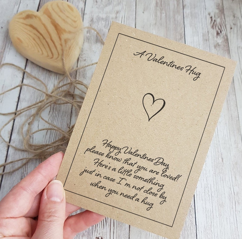 May include: A brown card with the text "A Valentines Hug" and a heart symbol. The card also has the text "Happy Valentines Day, please know that you are loved! Here's a little something just in case I'm not close by when you need a hug."