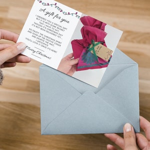 May include: A white card with a pink and blue patterned gift bag on it. The card has a message that reads "A gift for you I ordered you a special gift but it is with some regret that I have to say, though it's Christmas Day it's not been delivered yet... So enjoy the Christmas spirit and soak up the festive cheer and despite the wait, anticipate you'll love it once it's here! Merry Christmas".