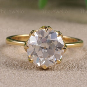 May include: A gold engagement ring with a large, round, clear gemstone. The ring is set with a prong setting and has a simple band.