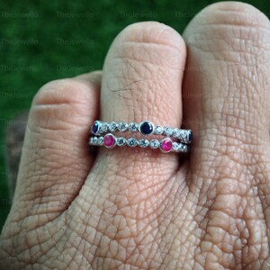 May include: Two silver rings with small gemstones. The top ring has five clear round stones and two blue round stones. The bottom ring has five clear round stones and two pink round stones.