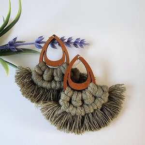 May include: A pair of green tassel earrings with brown wooden teardrop-shaped pendants. The earrings are handmade and feature a macrame design.