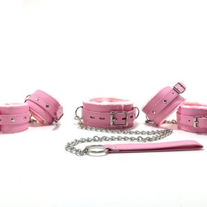 Op de afbeelding: Roze kunstbont gevoerde leren boeien met een zilveren ketting en bijpassende riem.