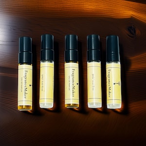 Pode incluir: Cinco pequenos frascos de perfume com tampas pretas e rótulos dourados, dispostos sobre uma superfície de madeira escura. Os rótulos dizem "Fragrance Maker EAU DE PARFUM" e "5ml/0.17 fl oz". Os frascos contêm um líquido âmbar claro.