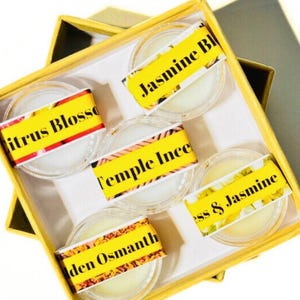 May include: A yellow box with five small glass jars containing scented wax melts. The jars are labeled with the scents: Citrus Blossom, Temple Incense, Golden Osmanthus, Jasmine Blossom, and Moss & Jasmine.