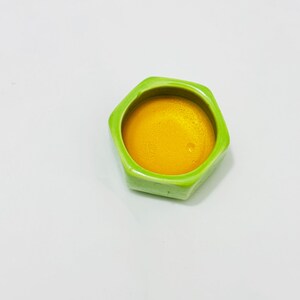 Close-up top view of golden Osmanthus solid perfume balm inside a lime green hexagonal ceramic jar. Rich, creamy beeswax texture with notes of sweet apricot and tea.