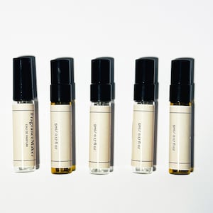 Puede incluir: Cinco pequeños frascos de perfume con tapas negras y etiquetas beige están alineados. Las etiquetas dicen "FragranceMaker EAU DE PARFUM" y "5ml / 0.17 fl oz". Los frascos contienen un líquido transparente.