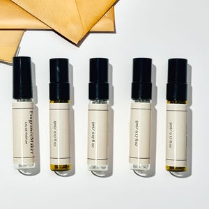 May include: Five perfume sample bottles with black lids and beige labels, each marked "5ml / 0.17 fl oz." The first bottle reads "FragranceMaker EAU DE PARFUM." A brown envelope is in the background.
