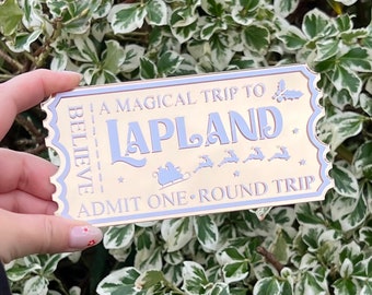 May include: A gold ticket with a blue border and the text "Believe" on the left side. The ticket says "A Magical Trip to Lapland" with a reindeer and sleigh illustration. The bottom of the ticket says "Admit One - Round Trip".