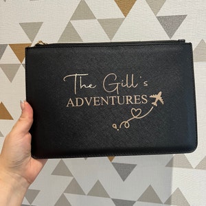 May include: Black zippered pouch with a gold zipper and the text "The Gill's Adventures" in gold lettering with a gold airplane and heart design.