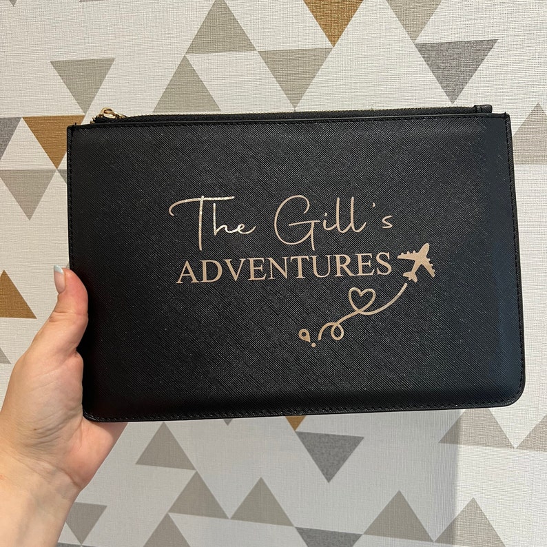 May include: Black zippered pouch with a gold zipper and the text "The Gill's Adventures" in gold lettering with a gold airplane and heart design.