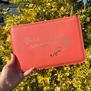 May include: A coral-colored zippered pouch with the text "Balchin Family Adventures" and a silver airplane with a heart trailing behind it.