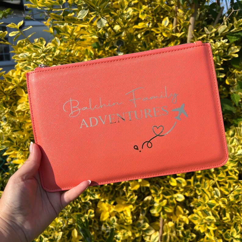 May include: A coral-colored zippered pouch with the text "Balchin Family Adventures" and a silver airplane with a heart trailing behind it.