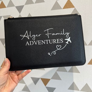 May include: Black zippered pouch with the text "Alger Family Adventures" and a small airplane graphic with a heart and a pin.