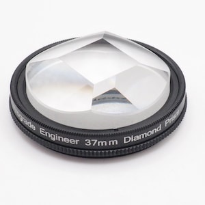 May include: A black 37mm diamond prism lens filter for photography. The filter is made of glass and has a black metal frame with the words "Engineer 37mm Diamond Prism" printed on it.