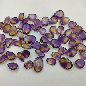 May include: A collection of amethyst and citrine gemstone drops, with a mix of purple and yellow hues. The stones are faceted and have a pear shape.