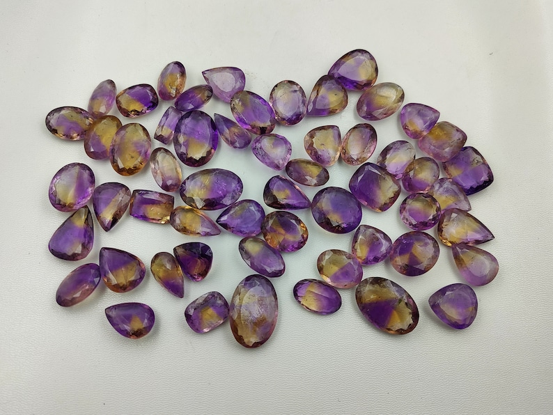 May include: A collection of amethyst and citrine gemstone drops, with a mix of purple and yellow hues. The stones are faceted and have a pear shape.