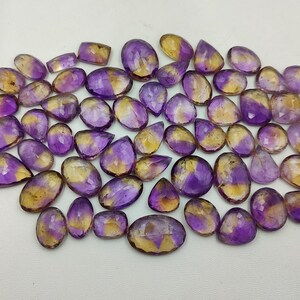 May include: A collection of 40 amethyst and citrine gemstone cabochons in various shapes and sizes. The stones are a mix of purple and yellow.