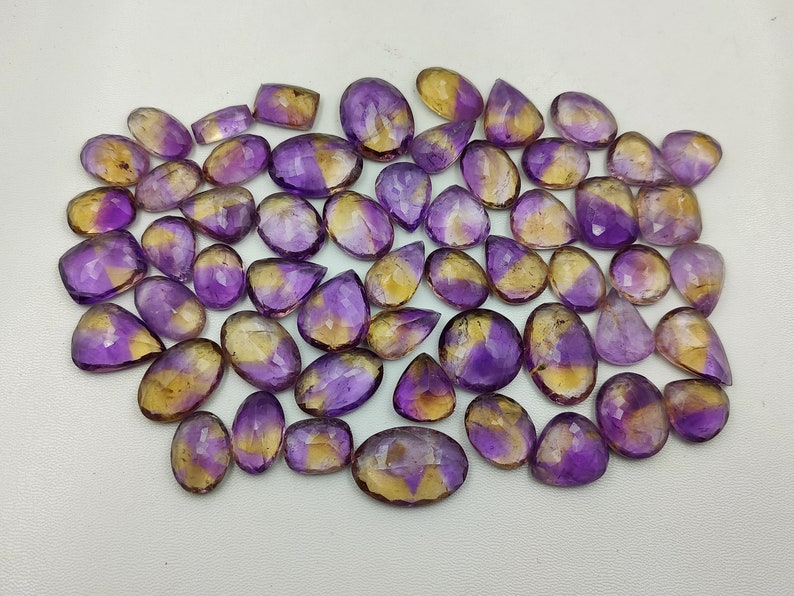 May include: A collection of 40 amethyst and citrine gemstone cabochons in various shapes and sizes. The stones are a mix of purple and yellow.