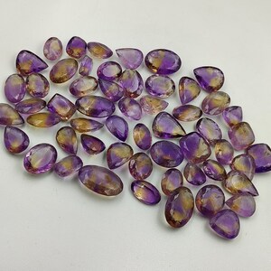 May include: A collection of 40 amethyst and citrine gemstone pear-shaped cabochons. The stones are a mix of purple and yellow.