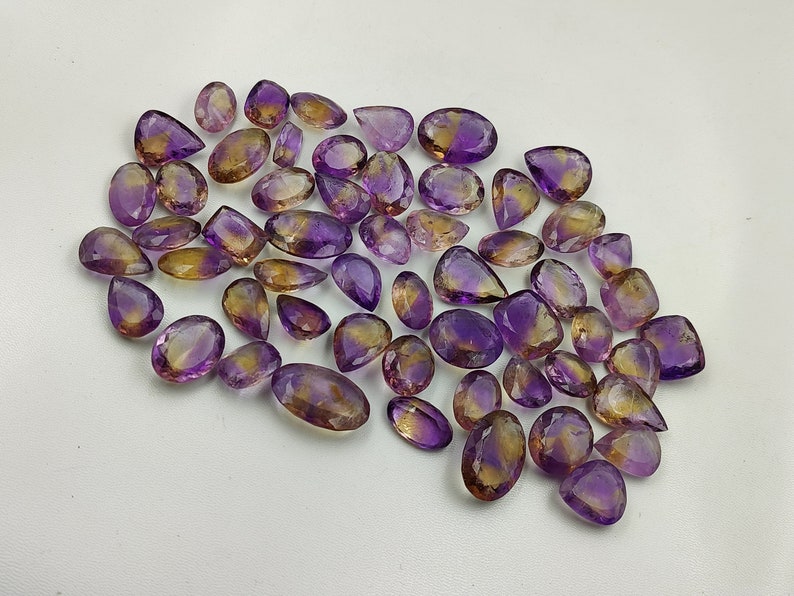 May include: A collection of 40 amethyst and citrine gemstone pear-shaped cabochons. The stones are a mix of purple and yellow.