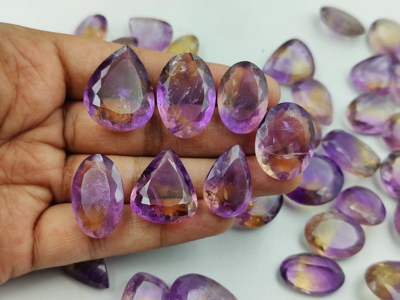 May include: A collection of amethyst and citrine gemstone drops, with a mix of purple and yellow hues. The stones are faceted and have a pear shape.