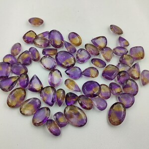 May include: A collection of 30 amethyst and citrine gemstone pear-shaped cabochons. The stones are a mix of purple and yellow.