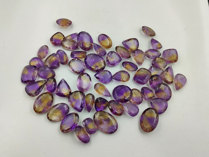 May include: A collection of 30 amethyst and citrine gemstone pear-shaped cabochons. The stones are a mix of purple and yellow.