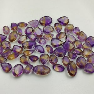 May include: A collection of amethyst and citrine gemstone pear-shaped drops. The stones are a mix of purple and yellow.