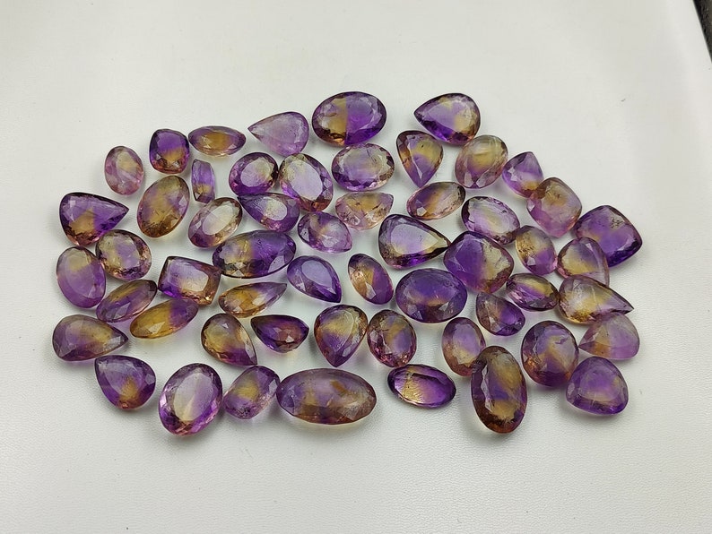 May include: A collection of amethyst and citrine gemstone pear-shaped drops. The stones are a mix of purple and yellow.