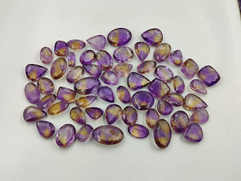May include: A collection of amethyst and citrine gemstone drops, with a mix of purple and yellow hues. The stones are faceted and have a pear shape.