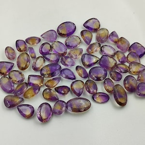 May include: A collection of amethyst and citrine gemstone drops, with a mix of purple and yellow hues. The stones are faceted and have a pear shape.