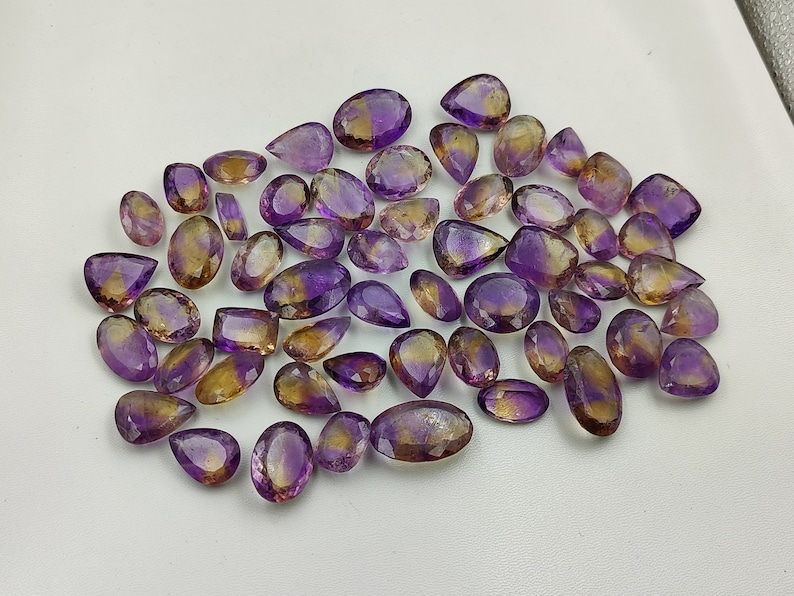 May include: A collection of amethyst and citrine gemstone drops, with a mix of purple and yellow hues. The stones are faceted and have a pear shape.
